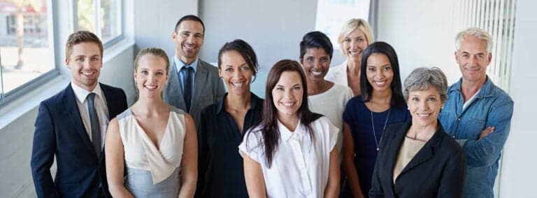 A smiling, diverse group of multi-generational business colleagues and executives standing together in a bright, modern office in Mt. Dora, Florida.