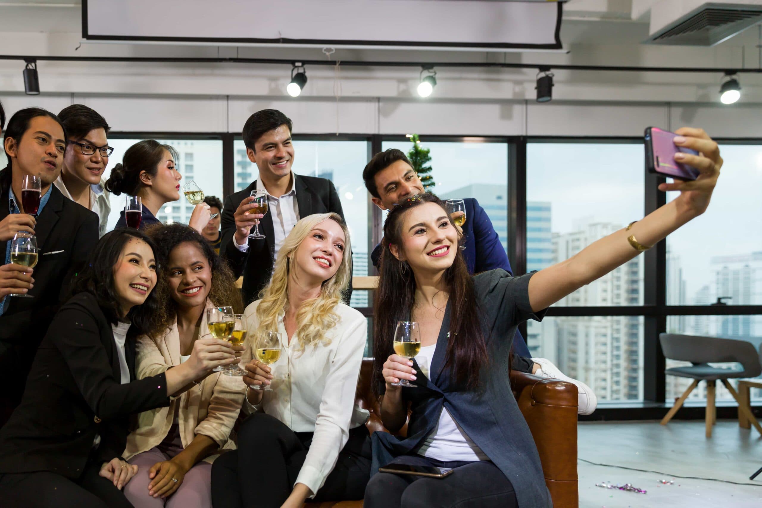 A diverse group of smiling professional colleagues taking a selfie and toasting with drinks during a corporate networking event in World Equestrian Center, Florida.