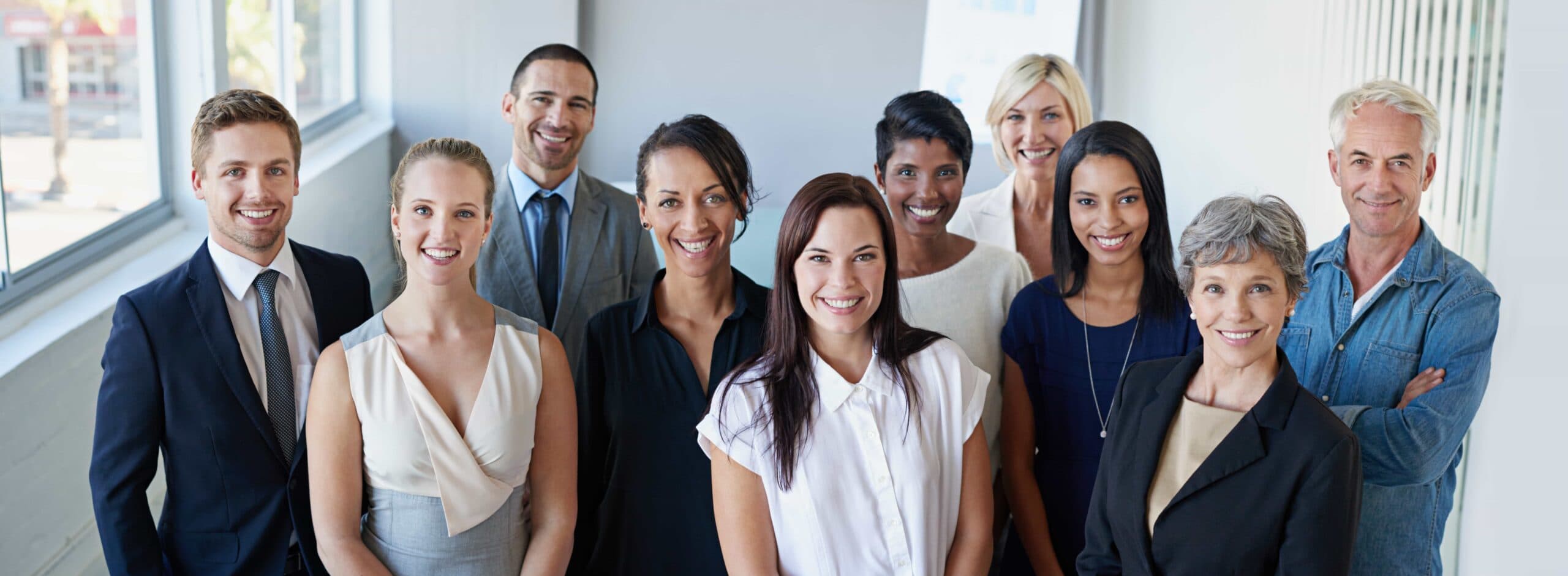 A smiling, diverse group of multi-generational business colleagues and executives standing together in a bright, modern office in Mt. Dora, Florida.