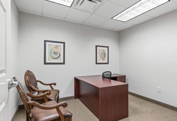 Plain office room with a wooden desk, a black chair, and two brown leather chairs. Walls are adorned with two nautical-themed artworks.